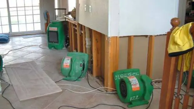 Green air movers set up to dry a wall cavity and floor